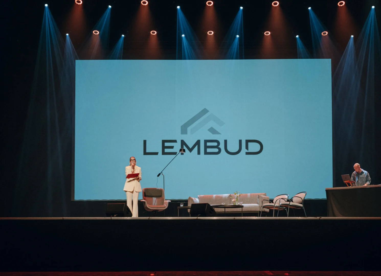 Scena z logo Lembud, prowadzącą w białym garniturze i DJ-em.