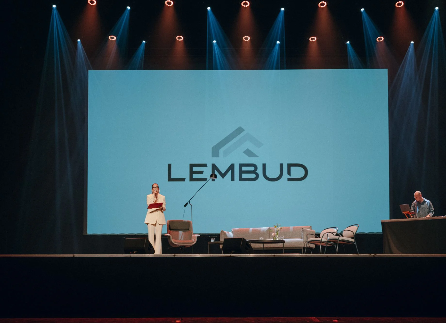 Scena z logo Lembud, prowadzącą w białym garniturze i DJ-em.